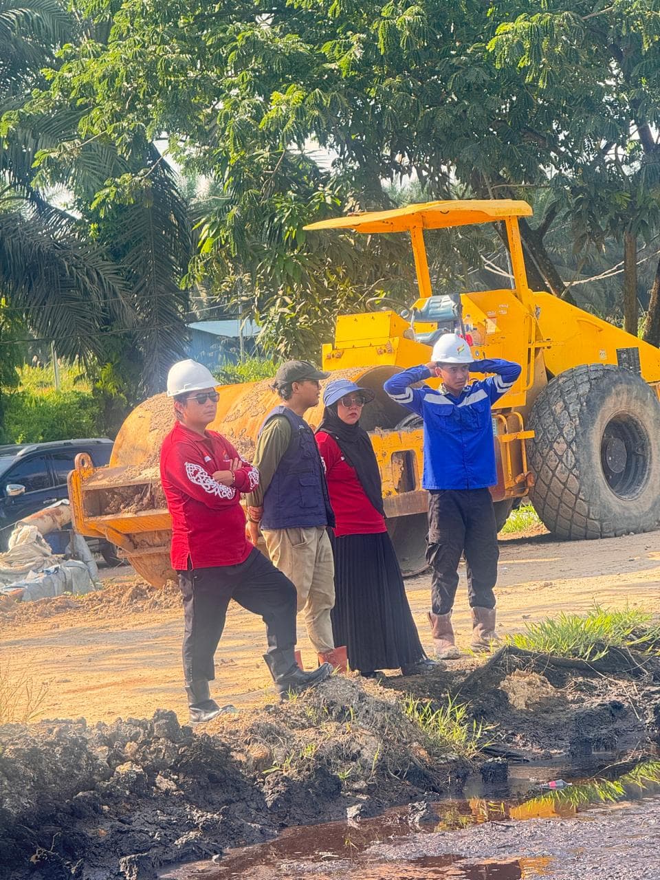 Tim lapangan dengan helm keselamatan mengawasi pemadatan dengan alat berat